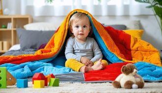 A young child sitting calmly under a colorful, textured weighted blanket in a peaceful room, highlighting the soothing effects of the blanket for children with autism.