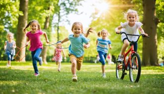 A lively group of children playing and participating in different outdoor activities in a park, symbolizing the benefits of physical activity for mental health.