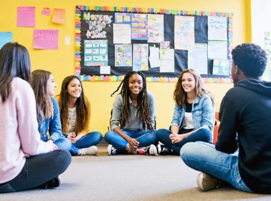 Diverse group of students engaging in a supportive circle discussion with a counselor in a school setting, illustrating a successful school mental health program.