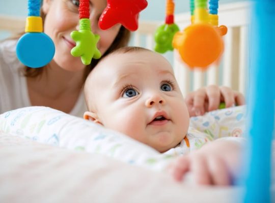 A curious baby observes a colorful, high-contrast mobile toy above their crib, highlighting the importance of visual stimuli in early childhood development with a parent gently engaging in the background.