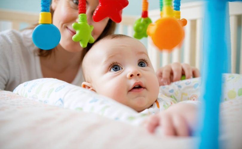 A curious baby observes a colorful, high-contrast mobile toy above their crib, highlighting the importance of visual stimuli in early childhood development with a parent gently engaging in the background.