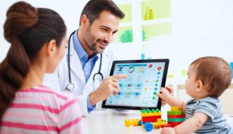 Healthcare provider explaining Z-codes to a parent in a clinic while a child plays with toys in the background.