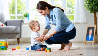 Parent kneeling and smiling while making eye contact with their child, emphasizing supportive and nurturing interaction in a home setting.