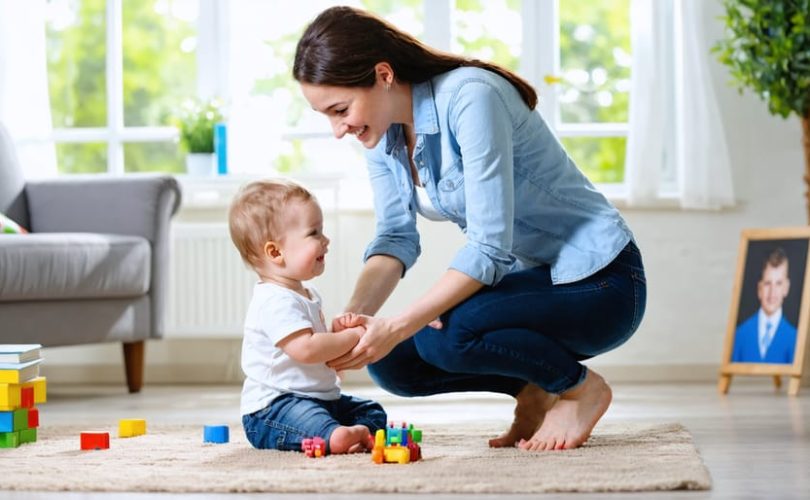 Parent kneeling and smiling while making eye contact with their child, emphasizing supportive and nurturing interaction in a home setting.